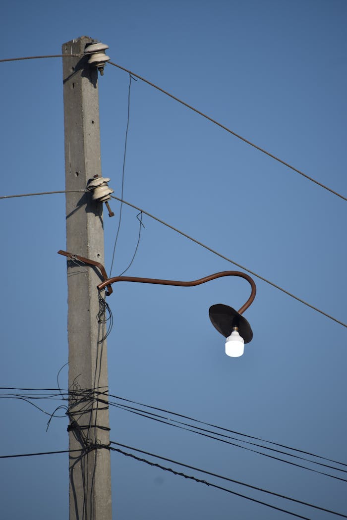 A close-up of a concrete electricity pole with a streetlight set against a clear blue sky.