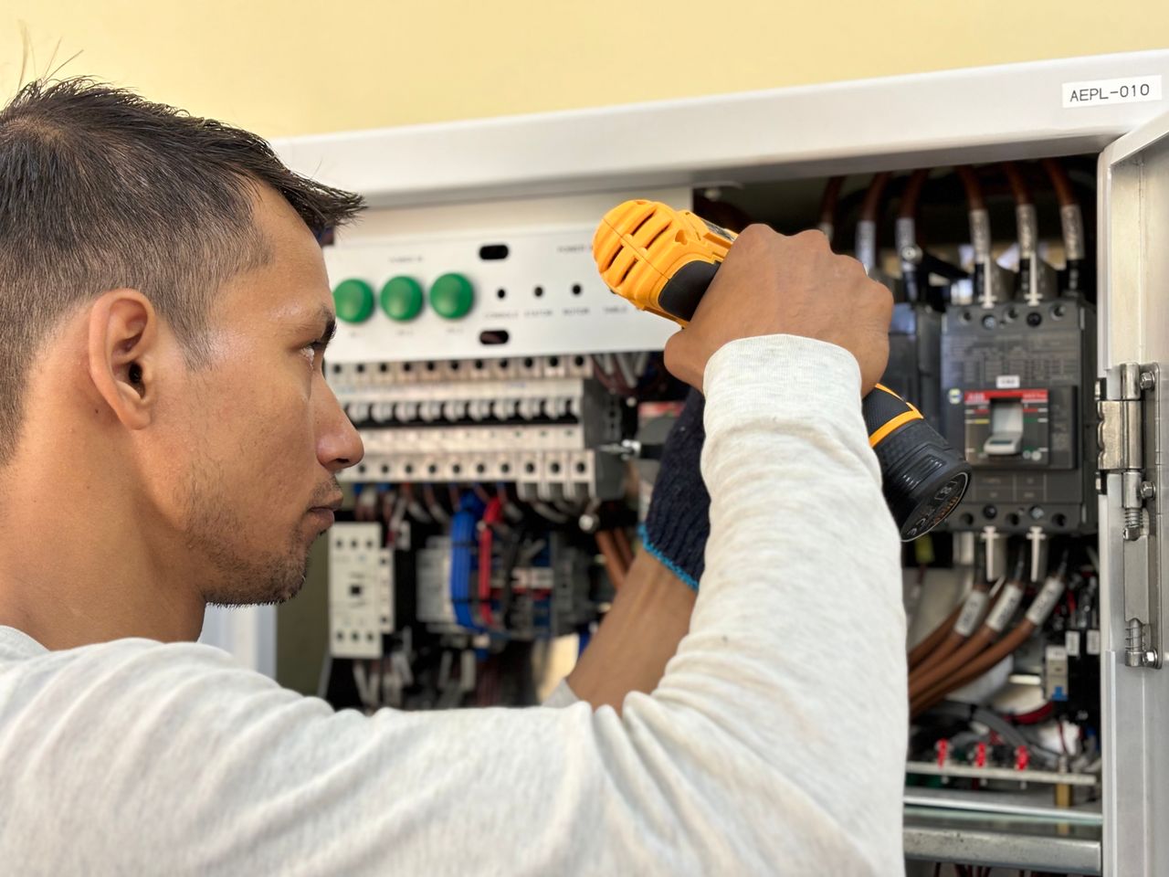 about-us Professional electrician using a drill on an indoor circuit breaker panel.