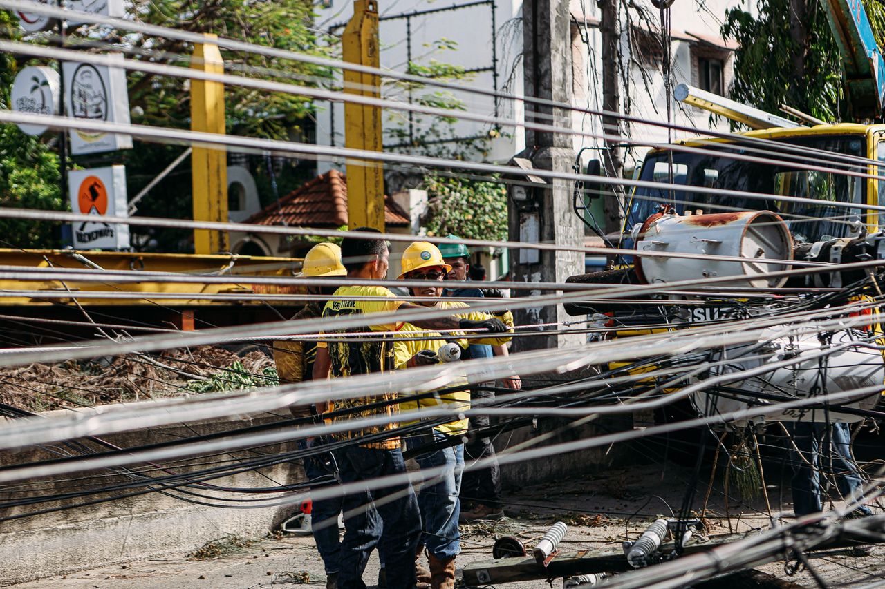 heros-img Utility workers repairing downed power lines amidst damaged infrastructure. Outdoor setting with chaos.