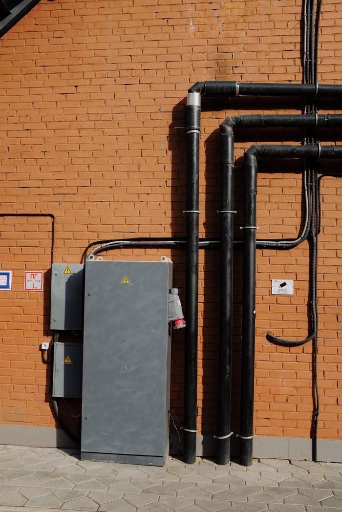 services-04 Outdoor scene showing electrical pipes and power box mounted on a brick wall.